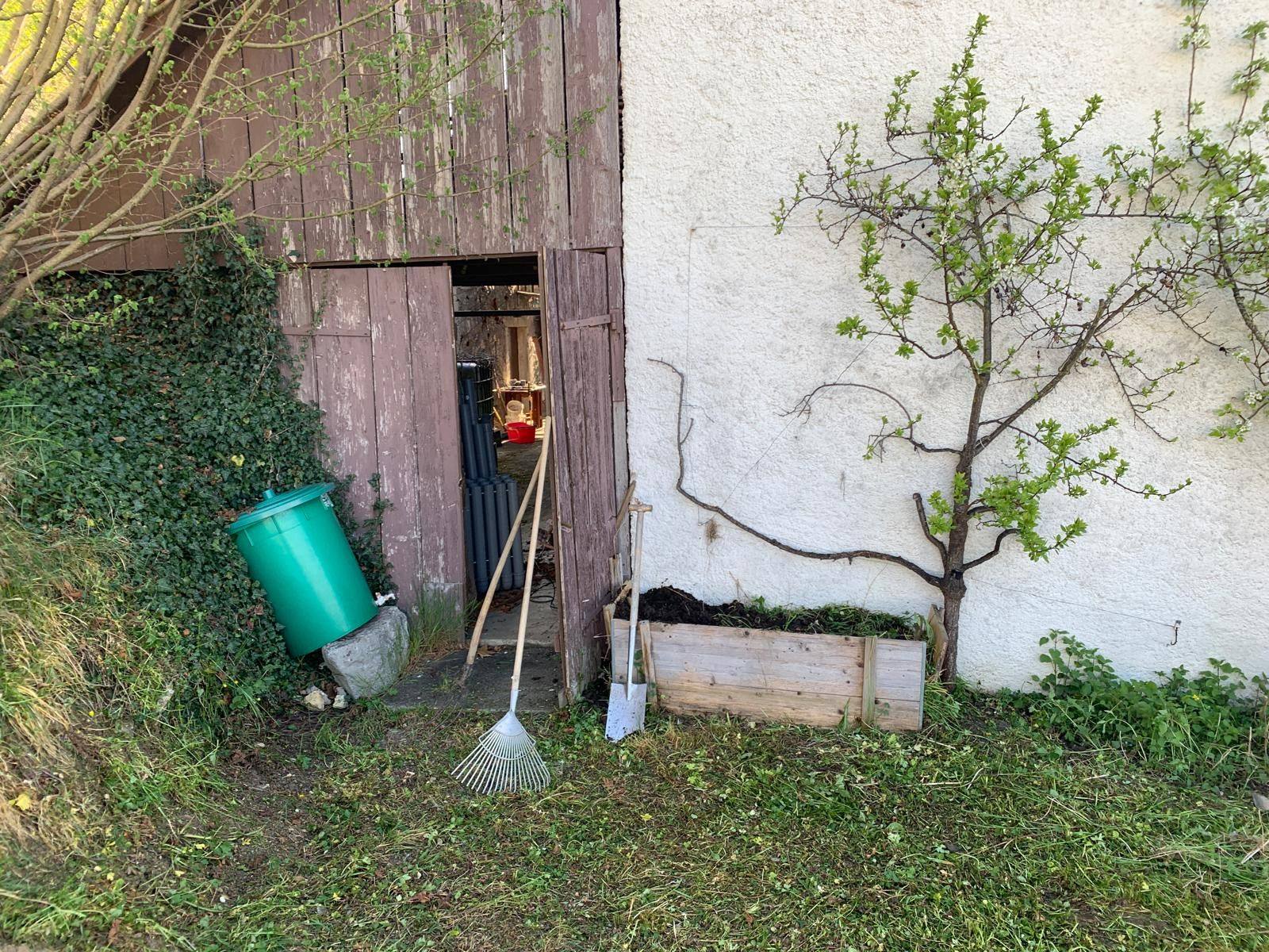 Schuppenwand mit Werkzeugen, grüner Tonne und Pflanzkasten